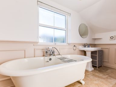 A bathroom with a white clawfoot bathtub under a window and a pedestal sink with a round mirror above at Tre Lowen in Port Isaac