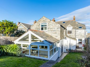 A stone house with a white conservatory and garden in the foreground at Tre Lowen in Port Isaac