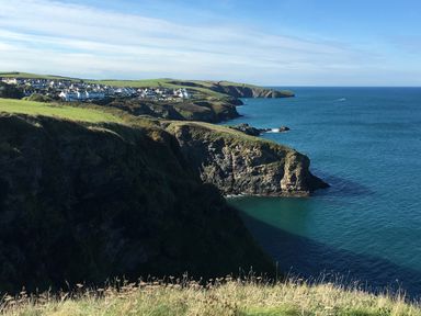 A coastal landscape with cliffs overlooking the sea and a village with houses on green fields at Tre Lowen in Port Isaac