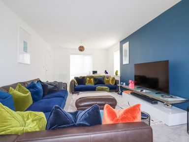 A living room with blue and green cushions on sofas and a television on a stand at Cobalt in St Eval near Mawgan Porth