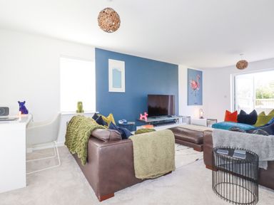 A living room with blue accent wall a television brown leather sofas and colorful cushions at Cobalt in St Eval near Mawgan Porth