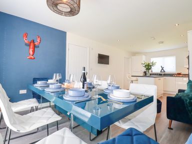A dining room with a blue dining table set for six and a kitchen in the background at Cobalt in St Eval near Mawgan Porth