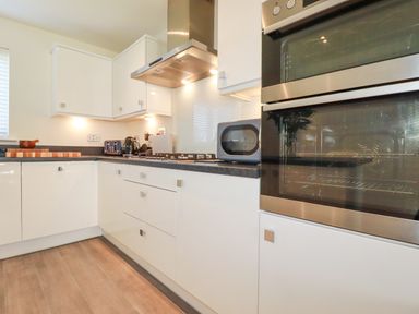 A kitchen with white cabinets a stove oven microwave toaster and kettle at Cobalt in St Eval near Mawgan Porth