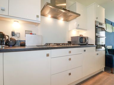 A kitchen with white cabinets a gas stovetop a microwave a double oven and small appliances on the counter at Cobalt in St Eval near Mawgan Porth