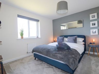 A bedroom with a bed with pillows and folded towels a mirror and bedside tables with lamps at Cobalt St Eval near Mawgan Porth