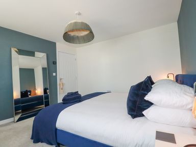 A bedroom with a large bed with white and blue bedding a full-length mirror against a blue wall and a pendant light at Cobalt in St Eval near Mawgan Porth