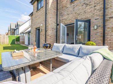An outdoor patio area with cushioned wicker seating and a glass-top table next to a brick house at Cobalt in St Eval near Mawgan Porth
