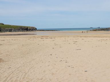 A wide sandy beach with some people walking near the water and rocky cliffs on the sides at Cobalt in St Eval near Mawgan Porth