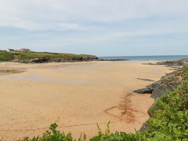 A sandy beach with rocky cliffs and some houses on grassy land near the shore at Cobalt in St Eval near Mawgan Porth