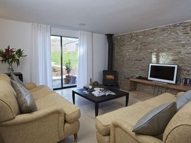 A living room with two beige sofas around a black coffee table and a wood stove against a stone wall at The Milking Shed in Bantham