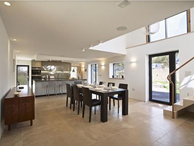 A dining area with a table set for six and an open kitchen with bar stools at The Milking Shed in Bantham