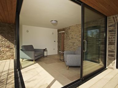 A seating area with two armchairs and side tables in a room with stone and white walls at The Milking Shed in Bantham