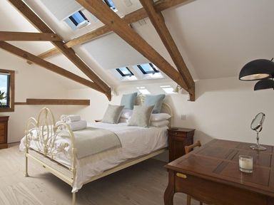 A bedroom with a metal bed frame wooden furniture skylights and exposed wooden beams at The Milking Shed in Bantham