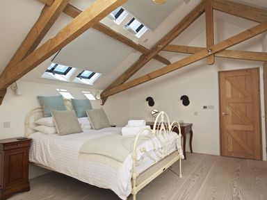 A bedroom with a bed white bedding wooden beams skylights and wooden door at The Milking Shed in Bantham