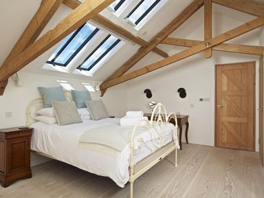 A bedroom with a bed under skylights and wooden beams with side tables at The Milking Shed in Bantham