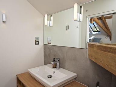 A bathroom sink with a mirror and wooden countertop with lights above at The Milking Shed in Bantham