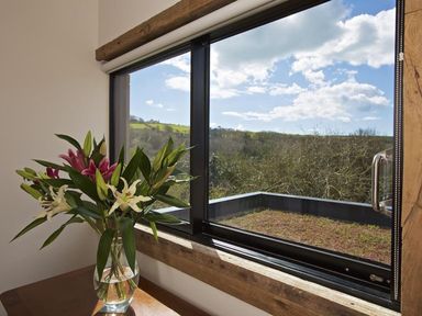 A vase with flowers on a table by a large window showing a view of hills and trees at The Milking Shed in Bantham