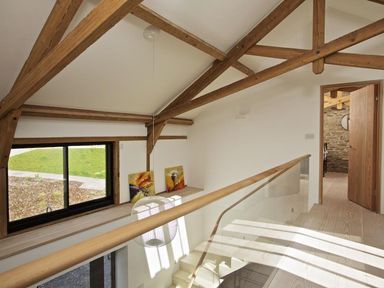 A staircase landing with wooden beams and glass railing overlooking the lower floor at The Milking Shed in Bantham