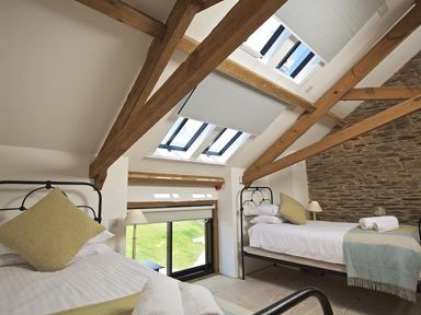 A bedroom with two single beds wooden beams skylights and a stone wall at The Milking Shed in Bantham