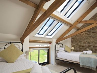 A bedroom with two single beds under skylights and exposed wooden beams at The Milking Shed in Bantham