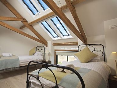 A bedroom with two single beds under skylights and wooden beams at The Milking Shed in Bantham