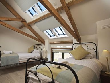 A bedroom with two single beds under skylight windows and wooden beams at The Milking Shed in Bantham