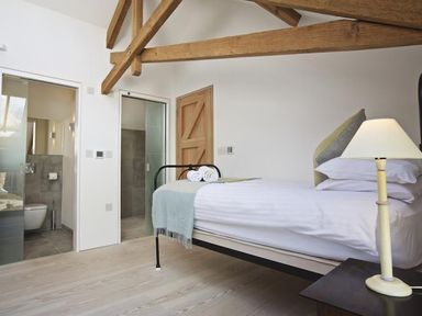 A bedroom with a bed, pillows, lamp, and exposed wooden ceiling beams at The Milking Shed in Bantham