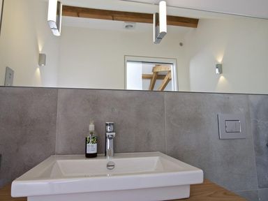A bathroom sink with a soap dispenser and a faucet below a mirror and wall lights at The Milking Shed in Bantham