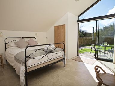 A bedroom with a bed near a sliding glass door leading to a patio with a table and chairs at The Milking Shed in Bantham