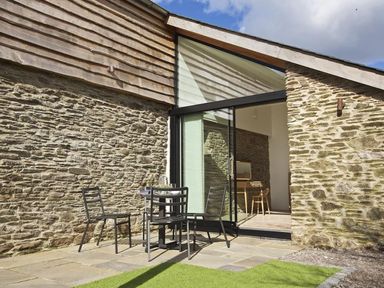 An outdoor seating area with a table and chairs on a stone patio next to a stone and wooden building at The Milking Shed in Bantham