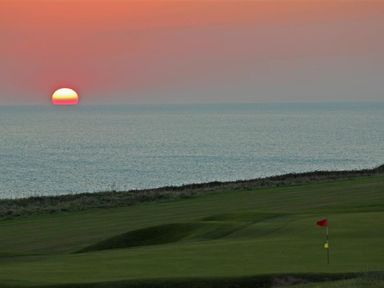 A golf course green with a flag near the coastline at sunset at The Milking Shed in Bantham