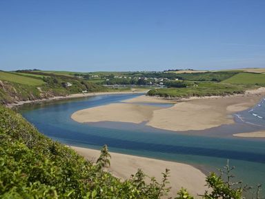 A coastal river flowing into the sea with sandbanks and green hills in the background at The Milking Shed in Bantham