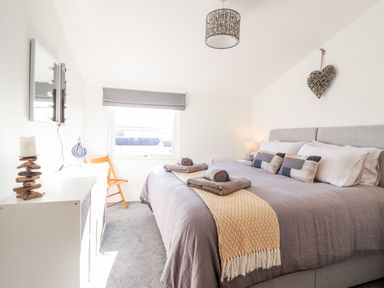 A bedroom with a large bed with folded towels on a blanket and a wooden chair near a window at Sea Breeze in Porthmadog