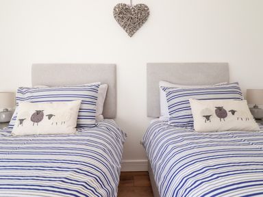 A bedroom with two single beds with striped bedding and sheep cushions at Sea Breeze in Porthmadog