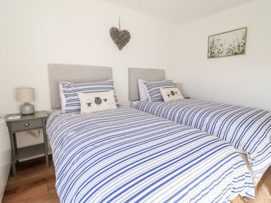 A bedroom with two single beds striped bedding and bedside tables with lamps at Sea Breeze in Porthmadog