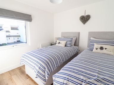 A bedroom with two single beds and striped bedding with a window on the left at Sea Breeze in Porthmadog