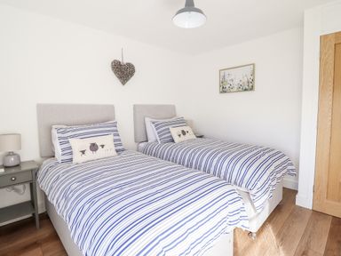 A bedroom with two single beds with striped bedding and a wooden floor at Sea Breeze in Porthmadog