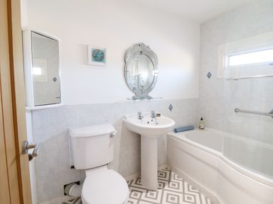 A bathroom with a toilet sink mirror bathtub and a small wall cabinet at Sea Breeze in Porthmadog