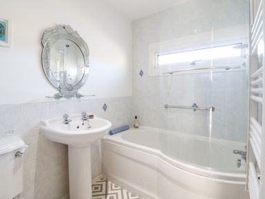 A bathroom with a pedestal sink a toilet a bathtub and a decorative mirror above the sink at Sea Breeze in Porthmadog