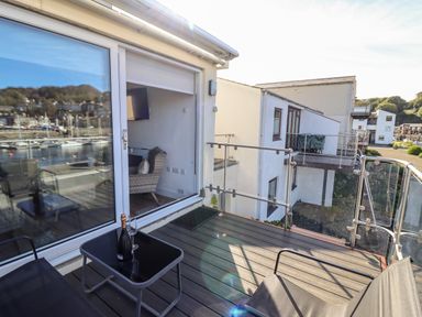 A balcony with a glass table holding a bottle and two glasses overlooking a marina at Sea Breeze in Porthmadog