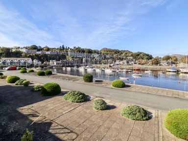 A marina with boats docked along the water and houses on a hill in the background at Sea Breeze in Porthmadog