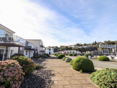 A walkway with shrubs and white buildings with balconies near a marina at Sea Breeze in Porthmadog