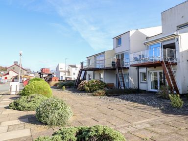 Exterior view of buildings with balconies stairs and bushes along a sidewalk at Sea Breeze in Porthmadog