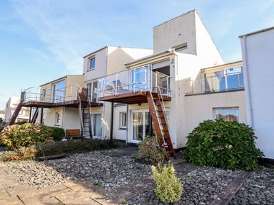 A modern multi-story building with balconies and stairs surrounded by shrubs and gravel at Sea Breeze in Porthmadog