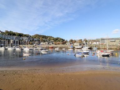 A harbor with boats docked near a shoreline and houses and hills in the background at Sea Breeze in Porthmadog
