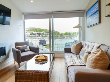 A living room with a sofa armchair glass coffee table and a balcony overlooking a marina at Sea Breeze in Porthmadog