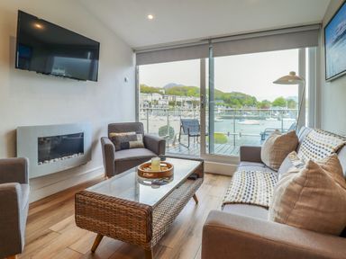 A living room with a sofa chairs coffee table wall-mounted tv and glass door overlooking a marina at Sea Breeze in Porthmadog