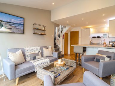 A living room with sofas, a wicker coffee table, kitchen area, and stairs at Sea Breeze in Porthmadog