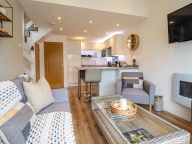 A living room with a grey sofa, armchair, coffee table, and kitchen area at Sea Breeze in Porthmadog