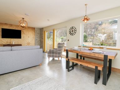 A living room and dining area with a gray sofa plaid armchair wooden dining table with bench and large window at Robins Downs in Ilfracombe